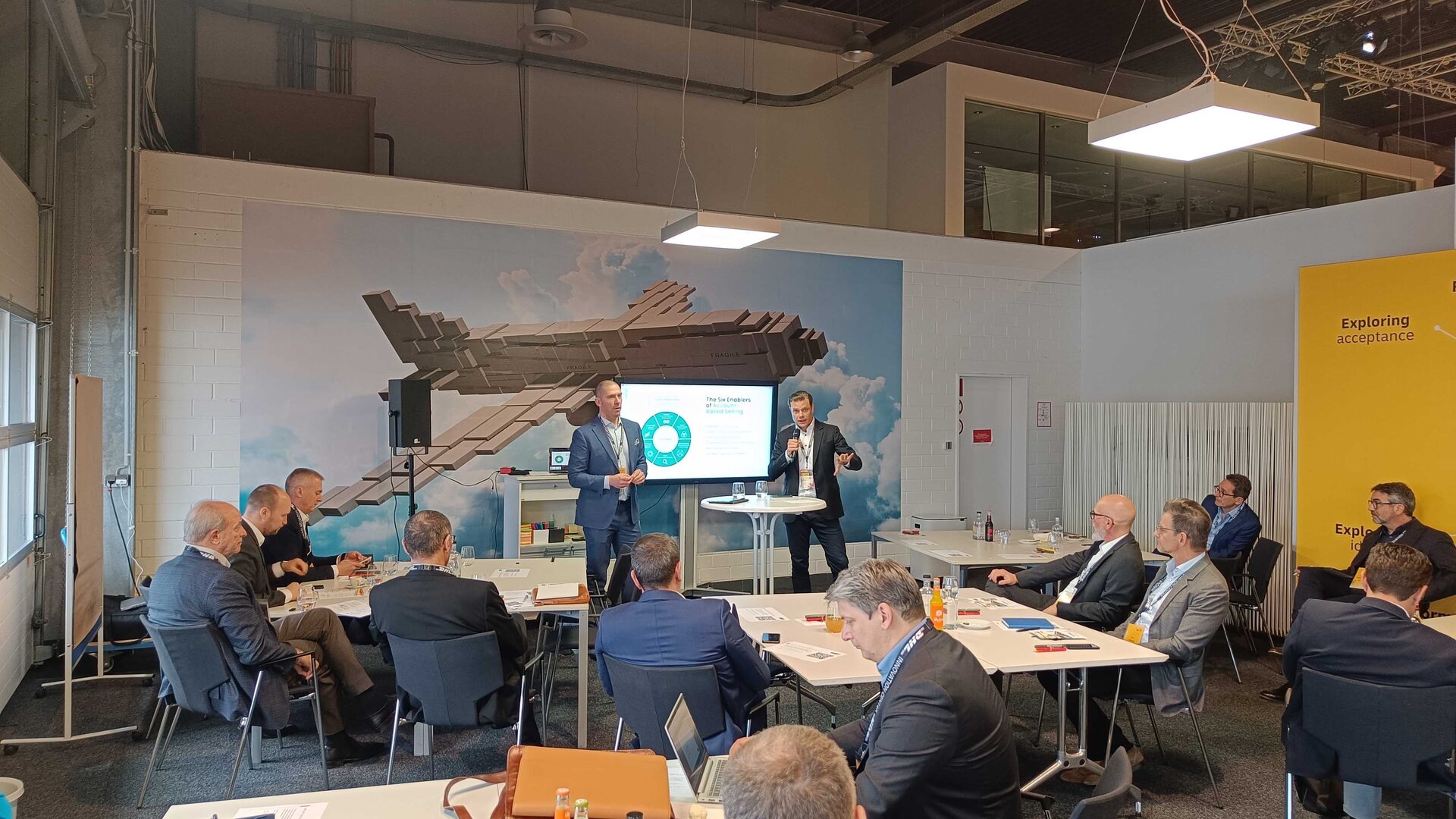 Christian Portmann (DHL) and Ulrik Monberg (ARPEDIO) on stage at the SAMA European Executive Symposium 2024, DHL Innovation Center in Troisdorf, with ARPEDIO's ABS Maturity Model on screen.